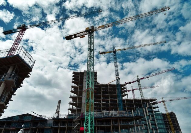 Large construction cranes against the backdrop of a partly cloudy blue sky.